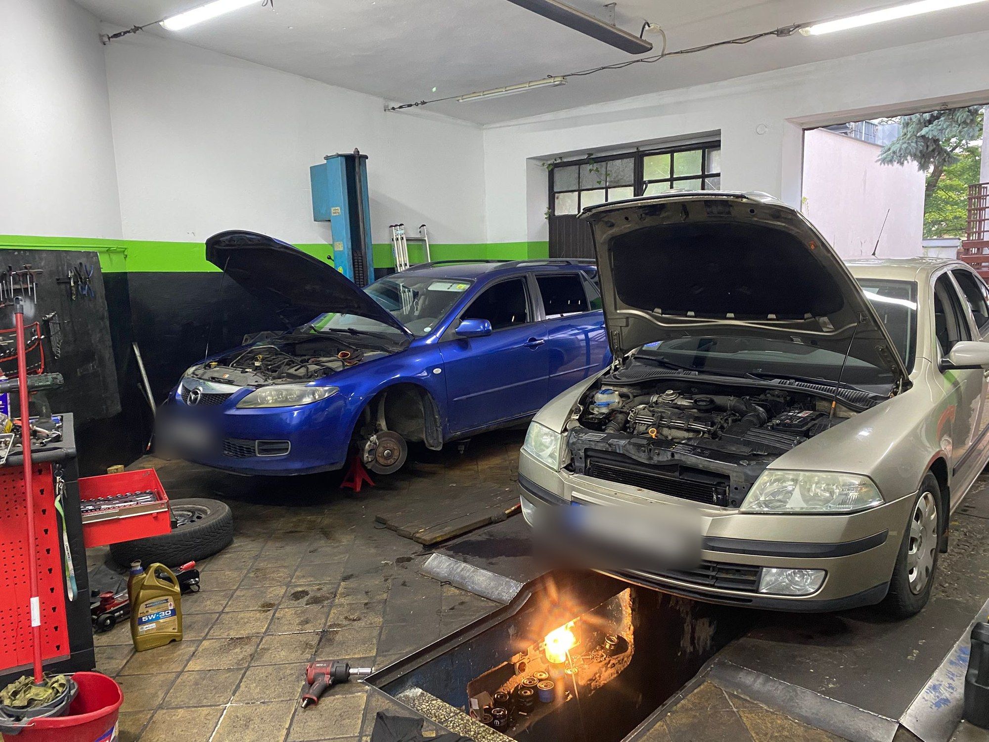 Wnętrze warsztatu Wasabi Service: Mazda na stanowisku i Skoda nad oświetlonym kanałem